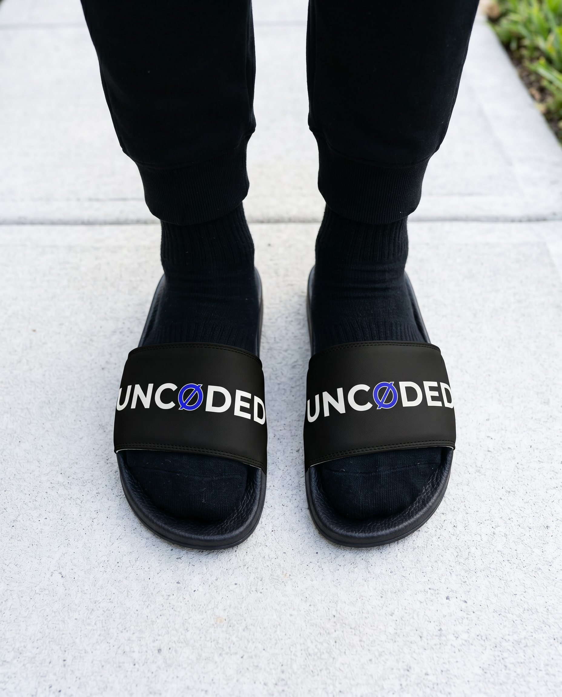 Person wearing UNCØDED Logo Slides black strap streetwear sandals front view #group:black-blue