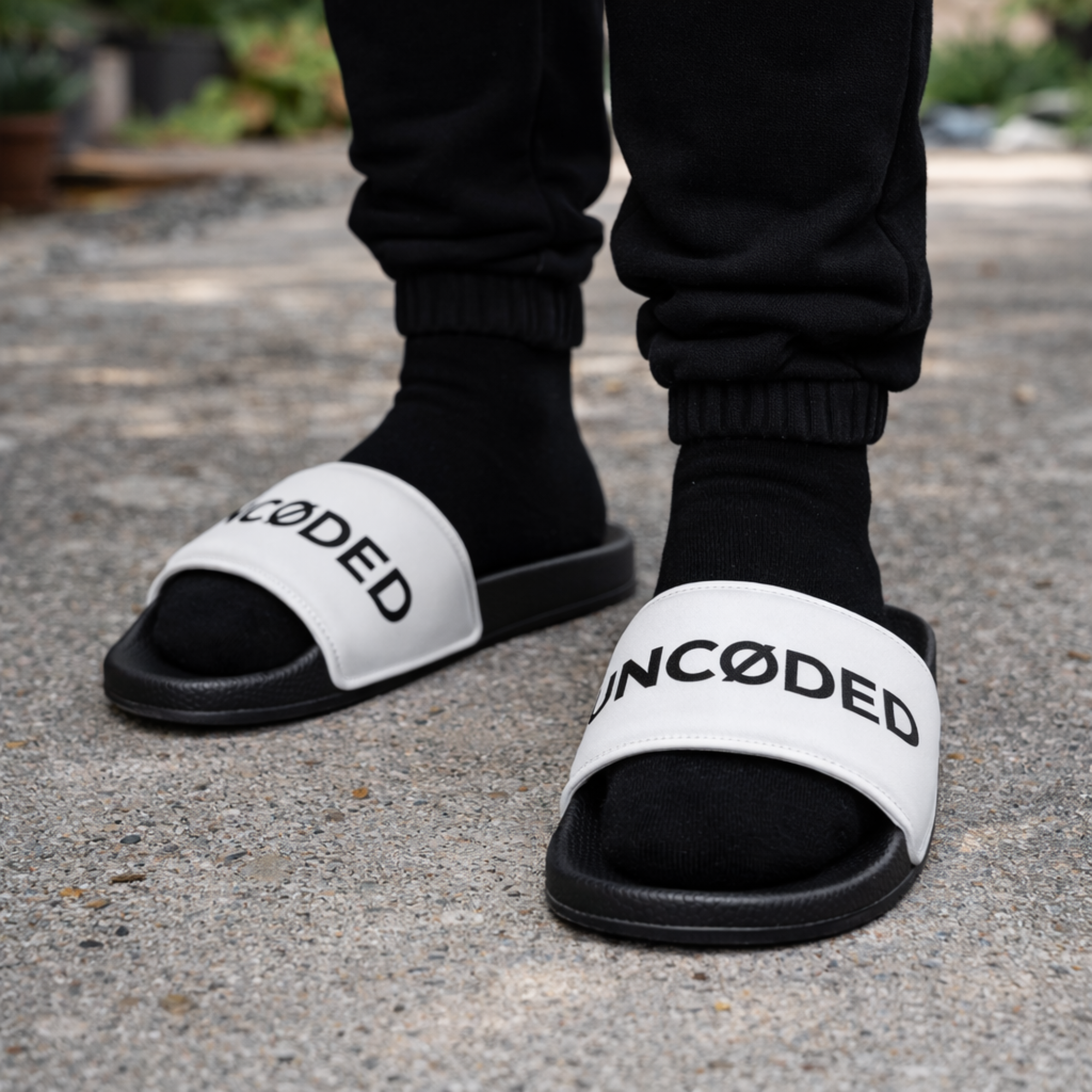 Person wearing UNCØDED Logo Slides white strap sandals on sidewalk #group:white-black