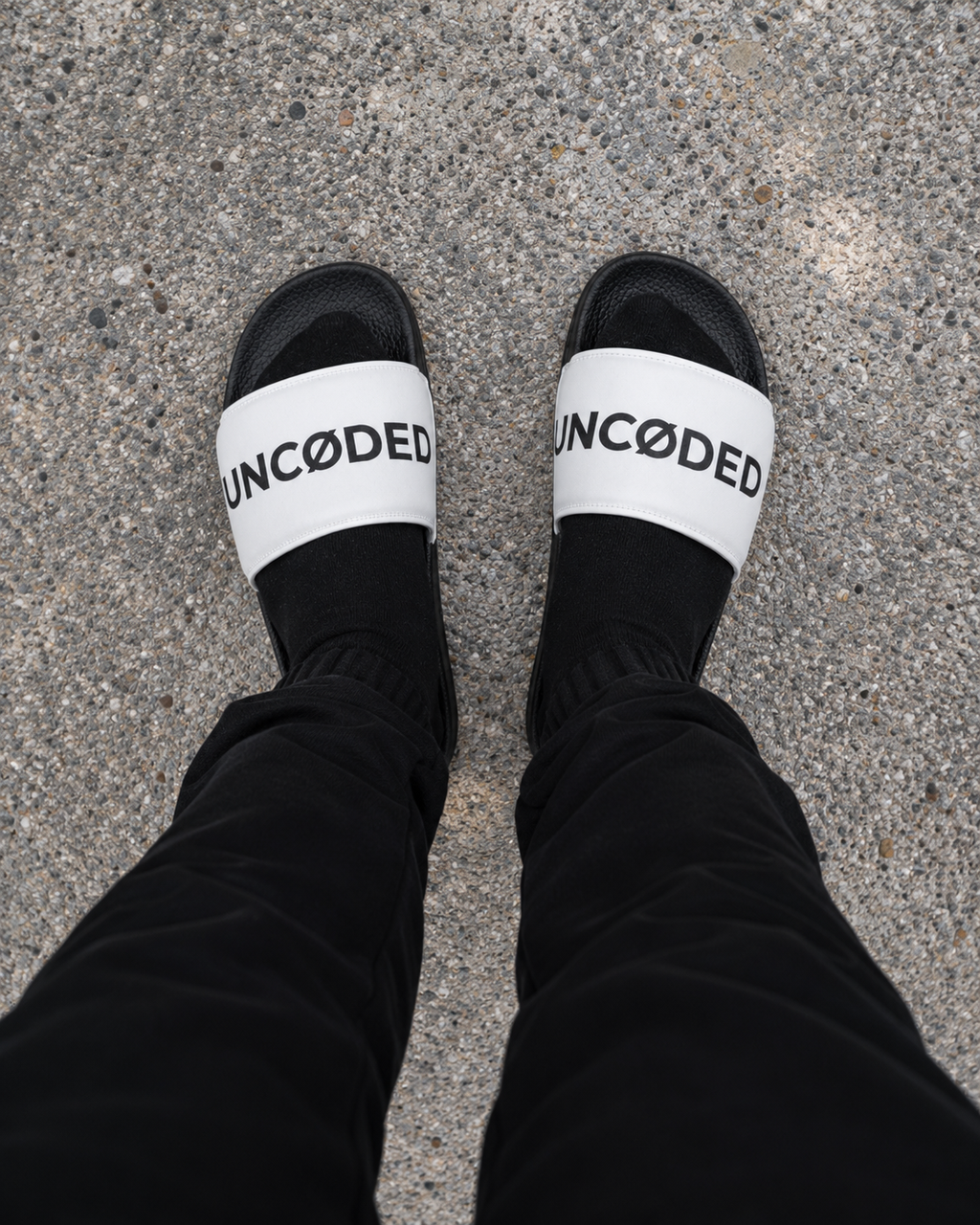 Person wearing UNCØDED Logo Slides white strap streetwear sandals top-down view #group:white-black