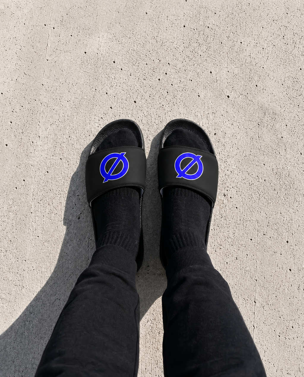 Person wearing UNCØDED Ø Slides with blue Ø logo top-down view #group:black-blue